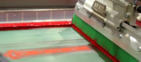 Green squeegee applying red ink on an Anatol screen printing machine, ensuring perfect pressure for vibrant prints